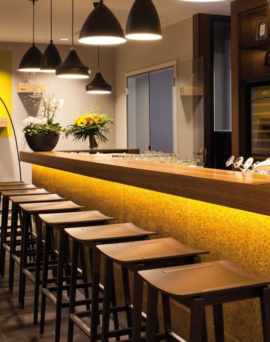 Blick auf Bartresen mit Barhockern und die Bar mit den Rueckwaenden im Hintergrund ein Ledersofa Farbe braun an der Wand stehend