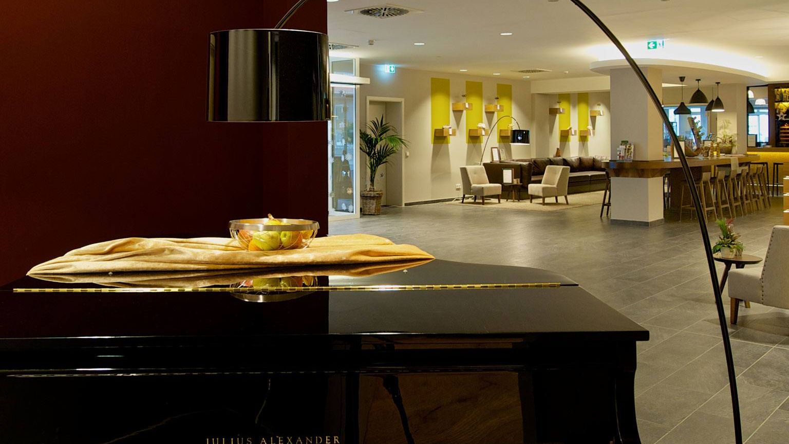 Blick vom schwarzen Piano aus in die Lobby mit Rezeption und den Designersitzmoebeln Neben dem Piano steht eine Designerleuchte in Schwarz Modell Twiggy