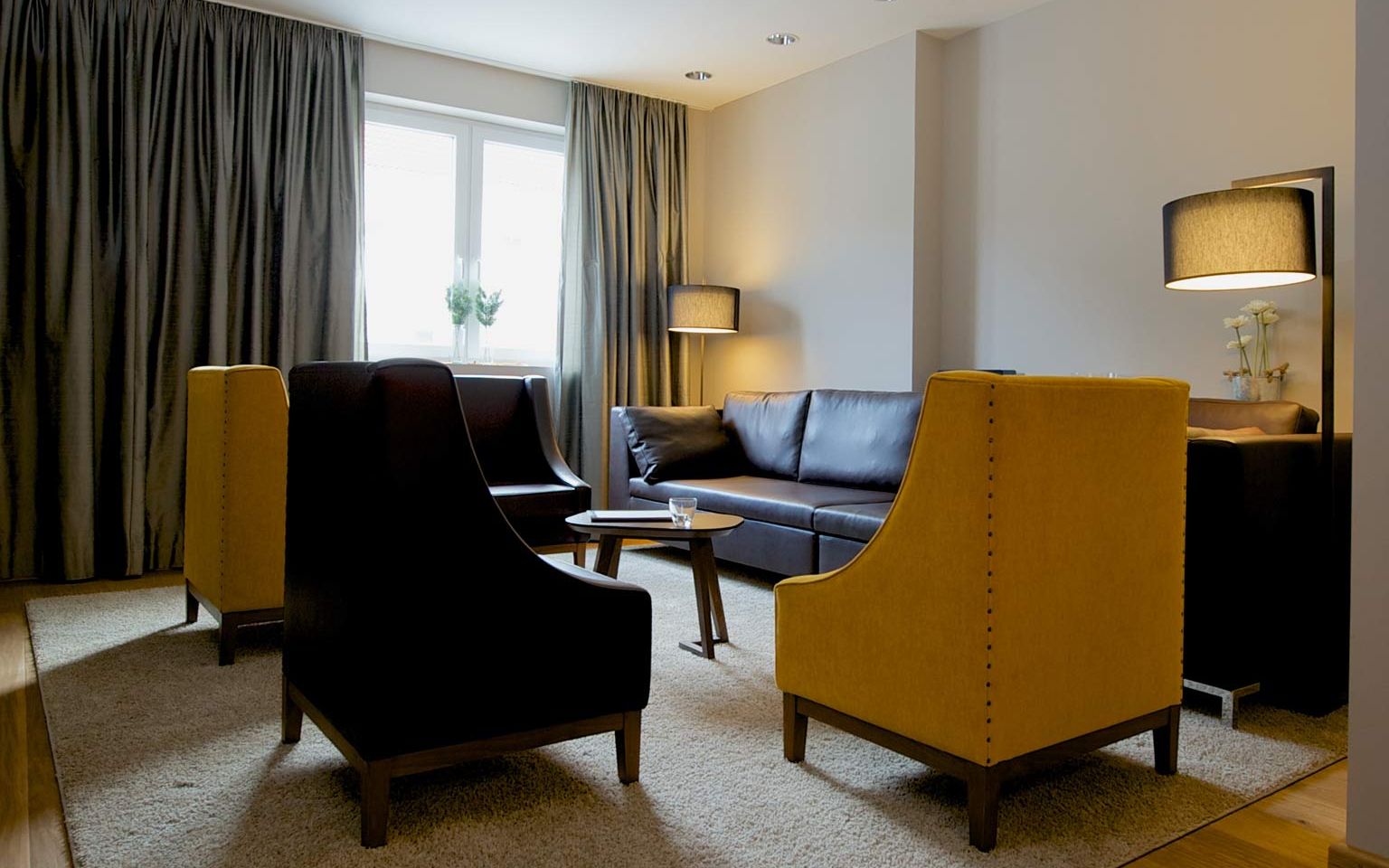 View of the master bedroom with three heavy leather armchairs, a leather couch, designer lamps and a solid wooden table