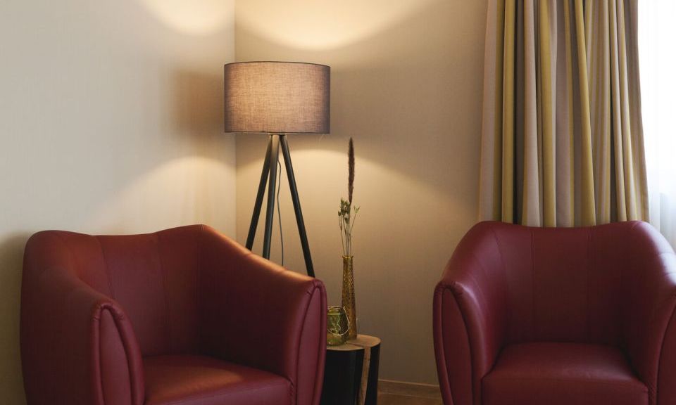 Blick auf zwei in weinrot gehaltene Armsessel mit Stehlampe in der Junior Suite der Kategorie Beerenauslese im Weinhotel Kaisergarten in Alzey
