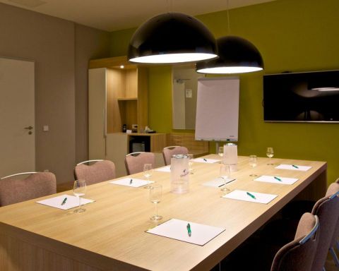 Tagungsraum Klassik Bestuhlung Blockform mit 8 Stuehlen, grosser TV an der Wand Designerleuchten ueber dem Tisch