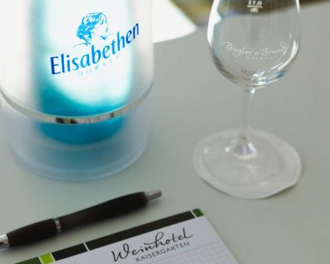 Schreibblock kariert mit Logo vom Weinhotel Kaisergarten und Stift, Wasserflasche und Glas auf dem Tagungstisch