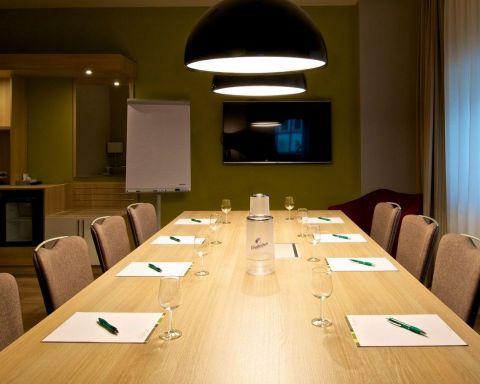 Tagungsraum Klassik Bestuhlung Blockform mit 8 Stuehlen, grosser TV an der Wand Designerleuchten ueber dem Tisch