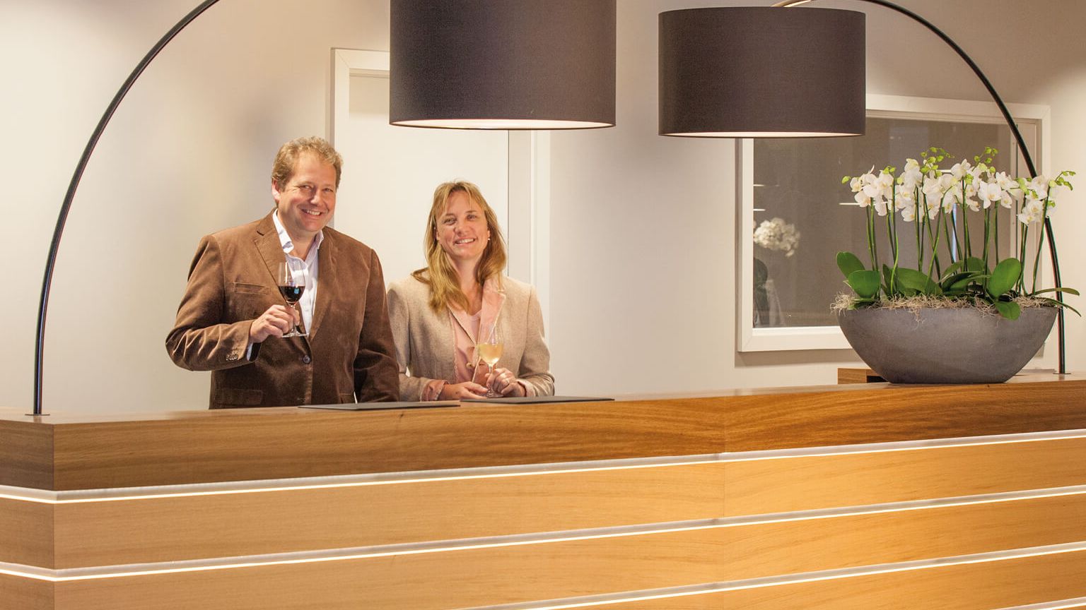 Petra Brand und Andreas Biegler hinter der Rezeption mit jeweils einem Glas Wein in der Hand