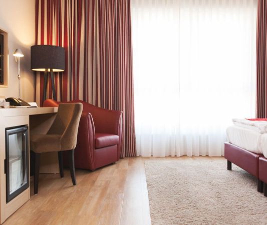 A view of the “Spätlese” double room at the Weinhotel Kaisergarten; in the foreground, wood-look laminate flooring - on the left, a desk, armchair, and TV - on the right, the double bed 