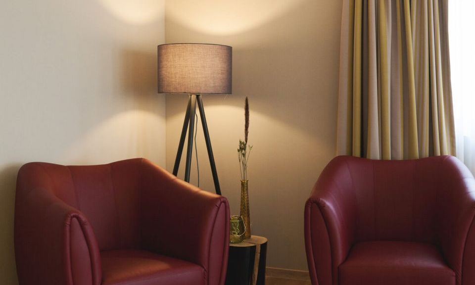 Blick auf zwei in weinrot gehaltene Armsessel mit Stehlampe in der Junior Suite der Kategorie Beerenauslese im Weinhotel Kaisergarten in Alzey