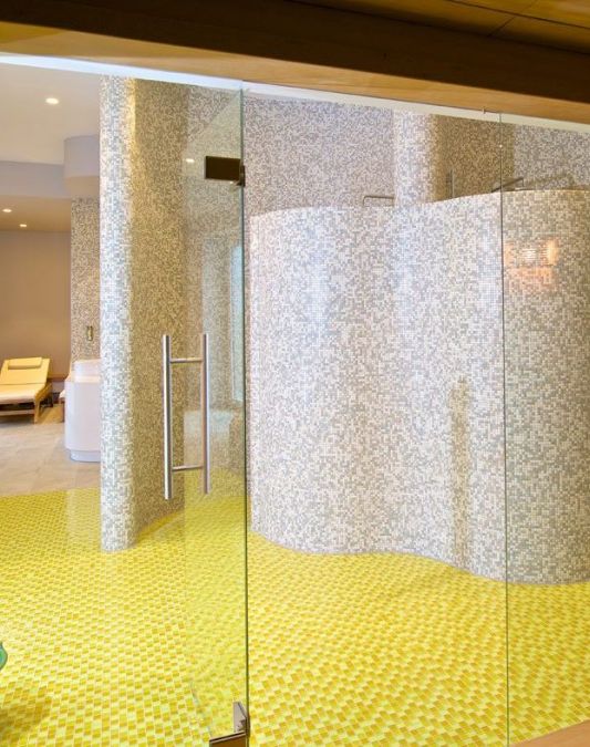 Ausblick aus der Sauna auf den in sonnigem gelb und beige gefliesten Nassbereich im Saunabereich des Weinhotel Kaisergarten in Alzey