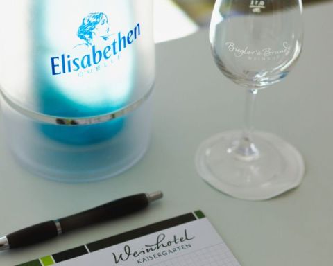 Writing pad chequered with logo of the Weinhotel Kaisergarten and pen, water bottle and glass on the conference table