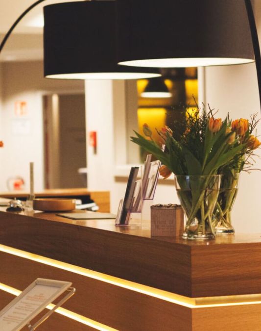A view of the reception desk at the Weinhotel Kaisergarten, illuminated by two black designer lampshades that form part of an arched light fixture