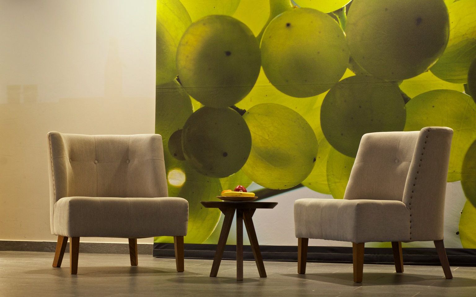 Two chairs and a small round table as designer furniture in the lobby of the Weinhotel Kaisergarten with a large photo of illuminated Riesling grapes on the wall