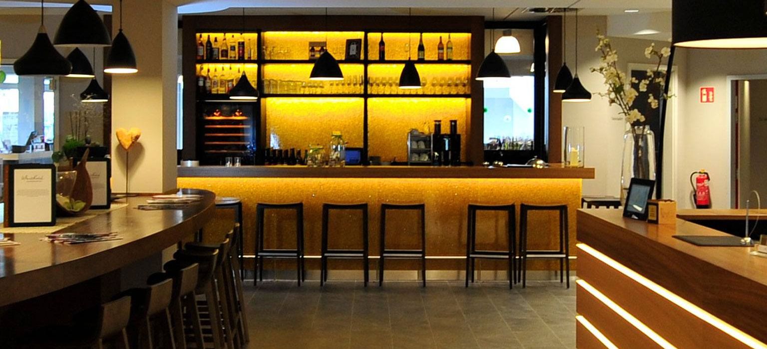 Frontal view from reception of the bar counter with the bar stools and the back wall of the bar, with the elliptical table for the bar guests cut off to the left