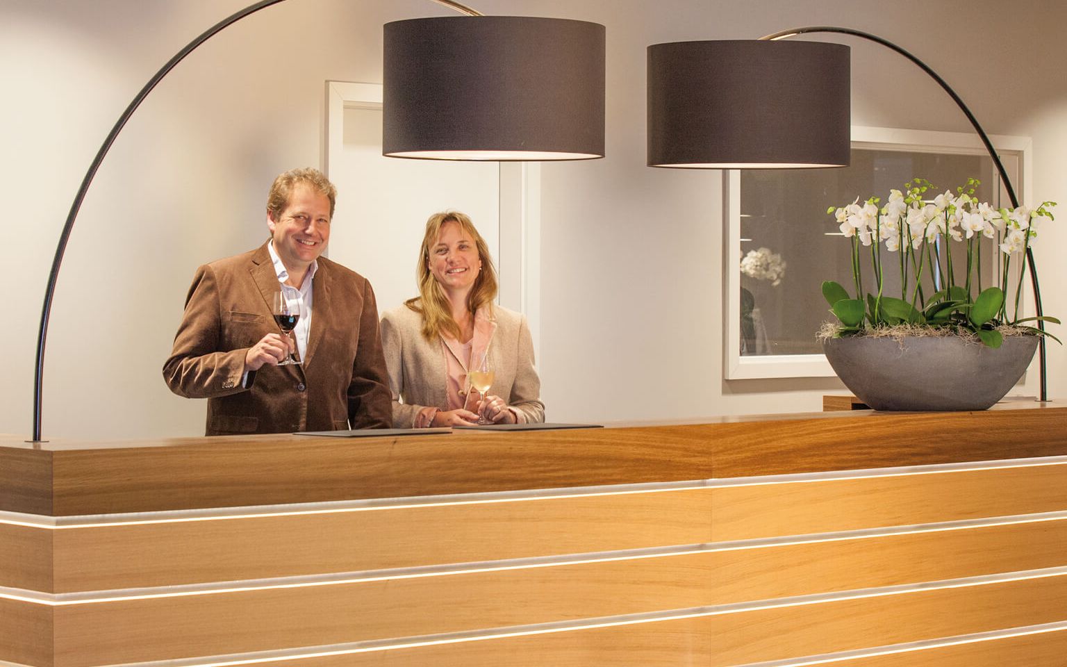 Petra Brand and Andreas Biegler behind the front desk, each holding a glass of wine