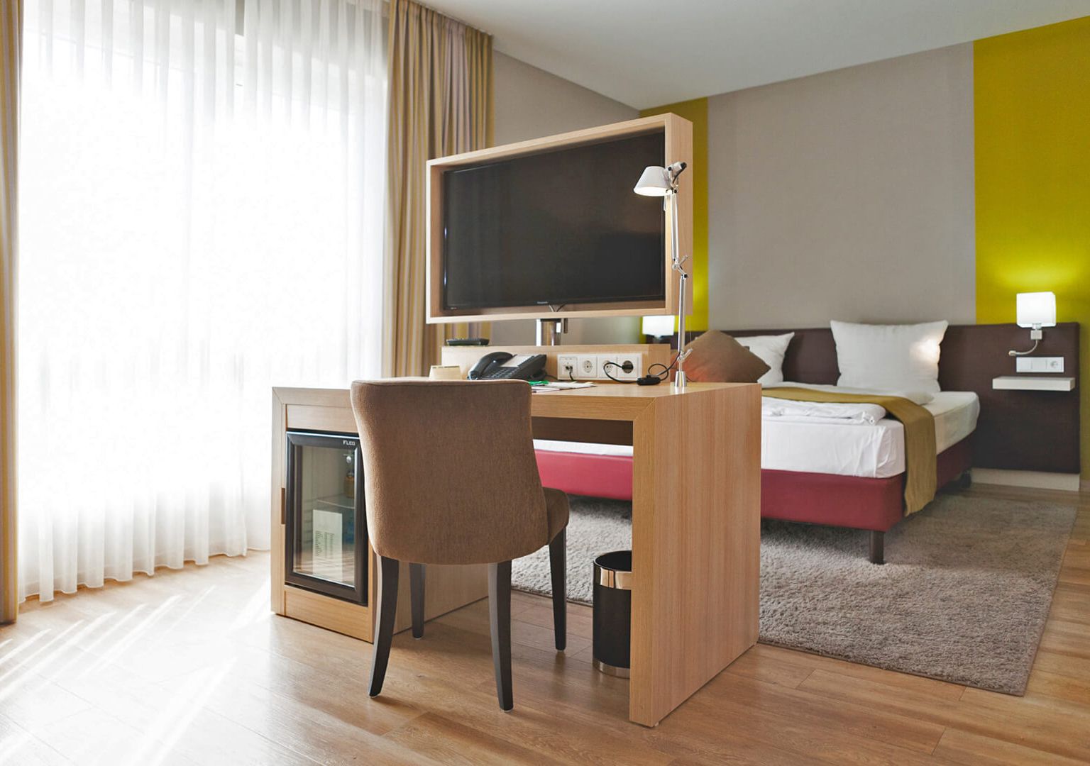 Blick in das Hotelzimmer der Kategorie Auslese im Weinhotel Kaisergarten in Alzey im Hintergrund das grosse Doppelbett und in der Mitte Schreibtisch mit drehbarem TV und Schreibtischstuhl  