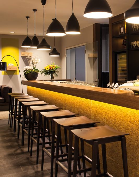 View of bar counter with bar stools and the bar with the back walls in the background a brown leather sofa standing against the wall