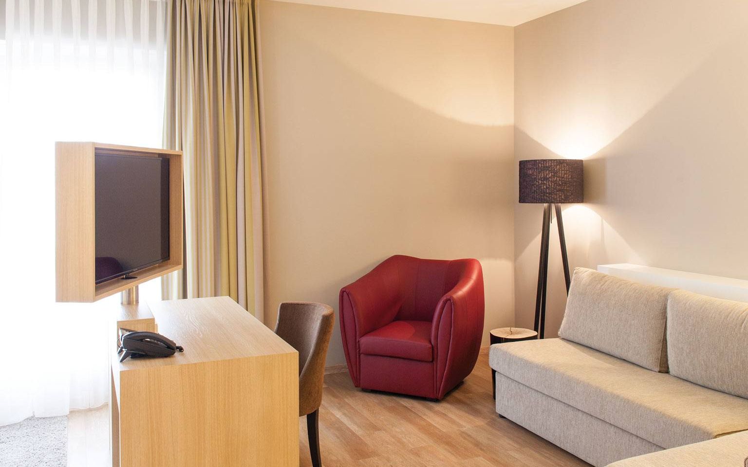 View of a wine-red armchair, floor lamp and the additional sofa bed for max. 2 smaller children up to 12 years in the category Auslese in the Weinhotel Kaisergarten in Alzey