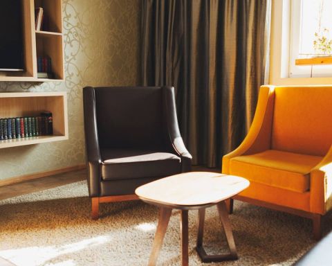 Blick in das Herrenzimmer als Tagungsraum mit drei schweren Ledersesseln eine Couch aus Leder Designerleuchten und ein uebergrosser Bildschirm fuer Praesentation oder TV