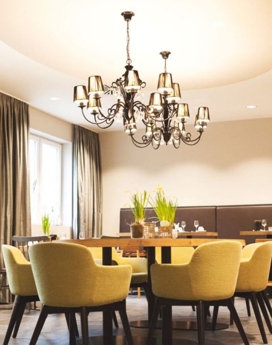 A view of the breakfast room at the Weinhotel Kaisergarten, seen from the buffet area, featuring wooden tables, several armchairs, and two designer chandeliers
