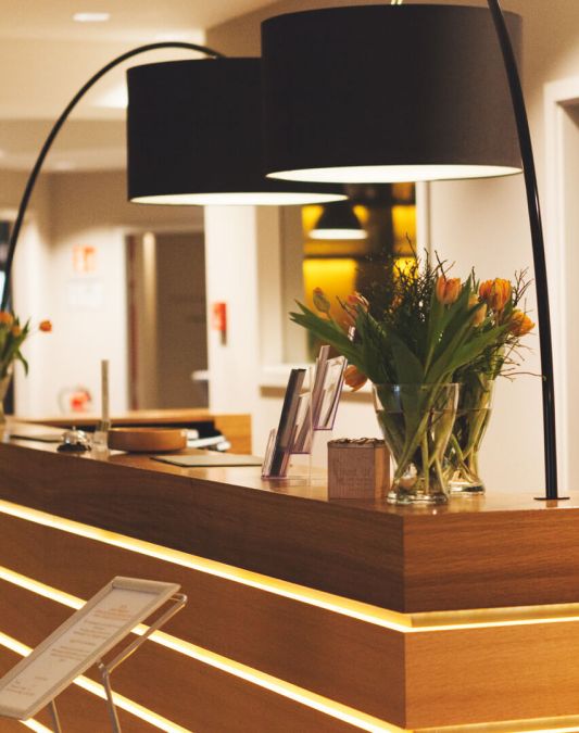 A view of the reception desk at the Weinhotel Kaisergarten, illuminated by two black designer lampshades that form part of an arched light fixture