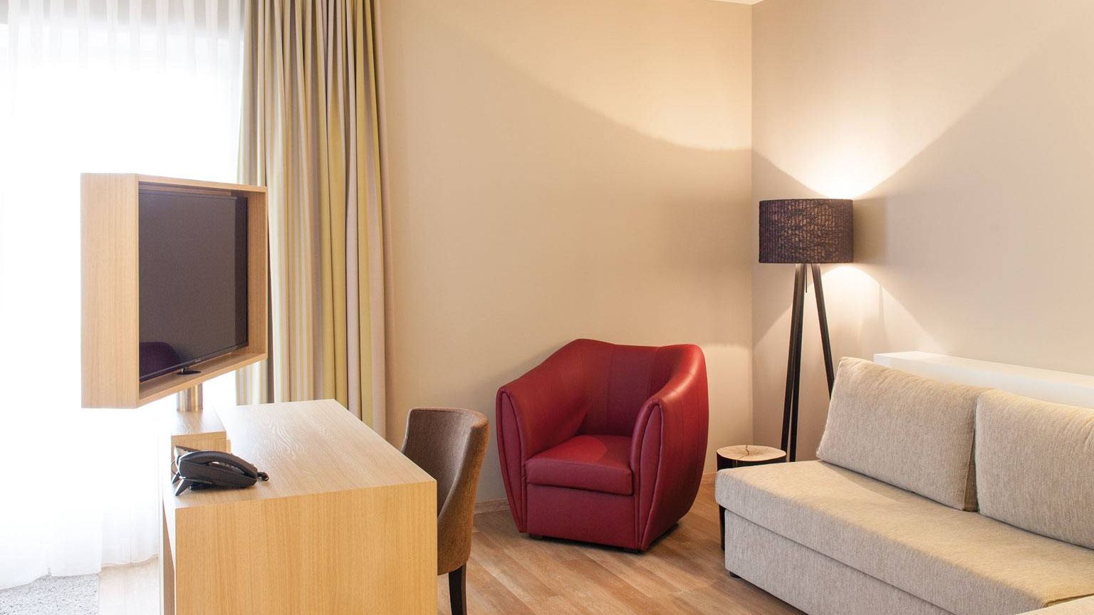 Blick auf einen weinroten Sessel, Stehlampe und die zusaetzliche Schlafcouch für max. 2 kleinere Kinder bis zu 12 Jahre in der Kategorie Auslese im Weinhotel Kaisergarten in Alzey