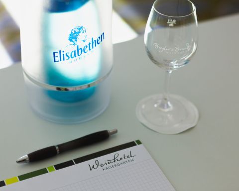 Writing pad chequered with logo of the Weinhotel Kaisergarten and pen, water bottle and glass on the conference table