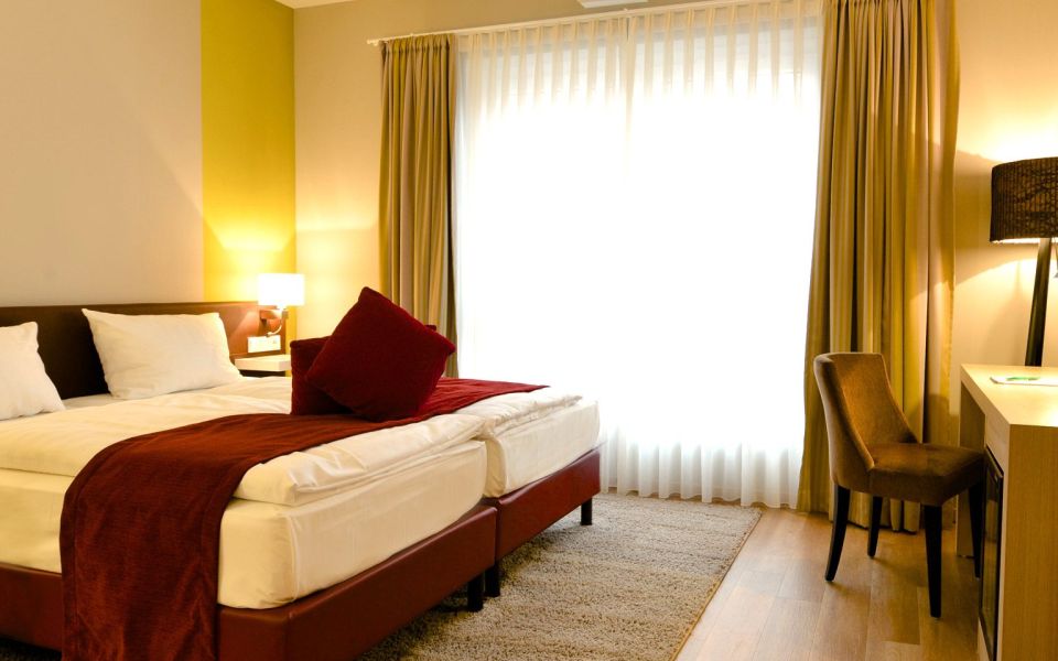 Rooms in the Spaetlese category at the Kaisergarten Alzey wine hotel View of the spacious double bed and desk with TV and minibar, dominated by the colours of the wine