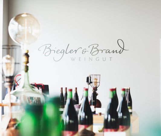 Wine shop and wine bar at the Weinhotel Kaisergarten in Alzey, with bottles of wine displayed in the foreground and the Biegler & Brand winery logo on the wall in the background