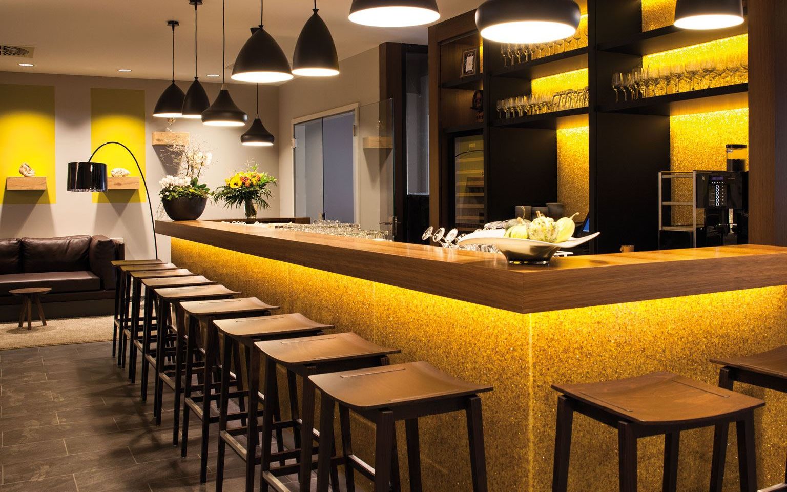 View of bar counter with bar stools and the bar with the back walls in the background a brown leather sofa standing against the wall