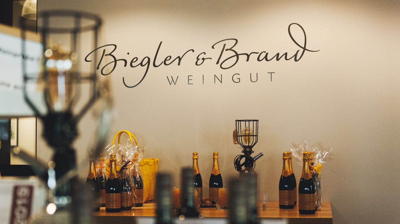 Flaschen mit Brut Sekt im Weinladen des Weinhotel Kaisergarten in Alzey - im Hintergrund das Logo des Weingut Biegler & Brand