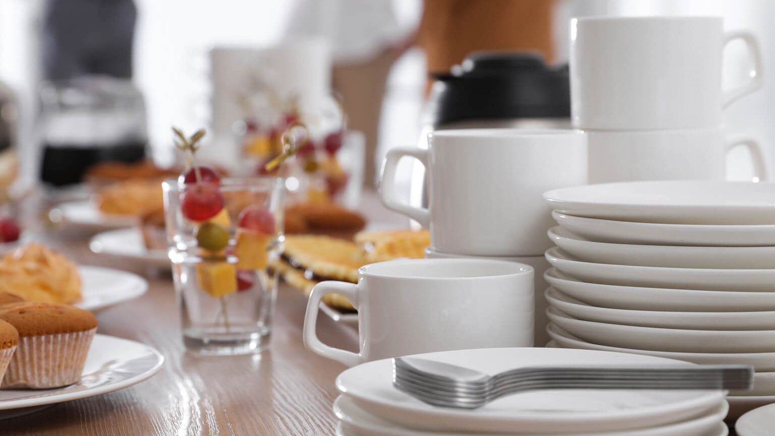 Set up for coffee break for conference participants saucers, coffee cups, plates, spoons, forks, thermos flask various sweet snacks arranged on a wooden table