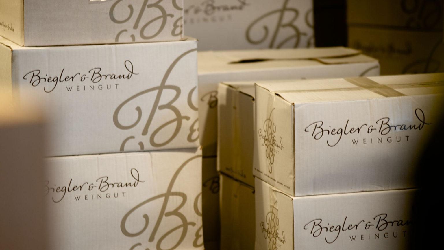 Gestapelte Weinkisten aus weißem Karton mit dem Logo des Weingut Biegler & Brand