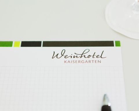 Writing pad chequered with logo of the Weinhotel Kaisergarten and pen tip on the conference table